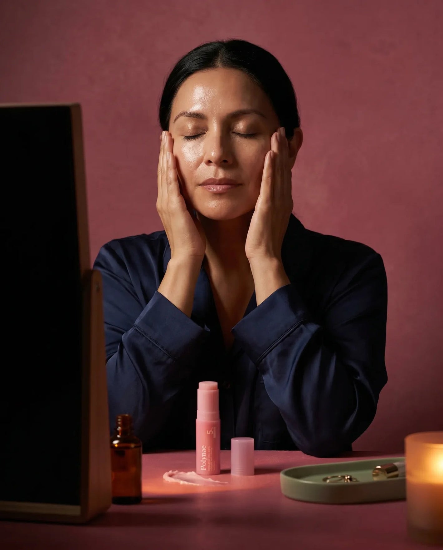 Young woman in purple sweatshirt rubbing Polynae product between her palms, seated on a pink stool