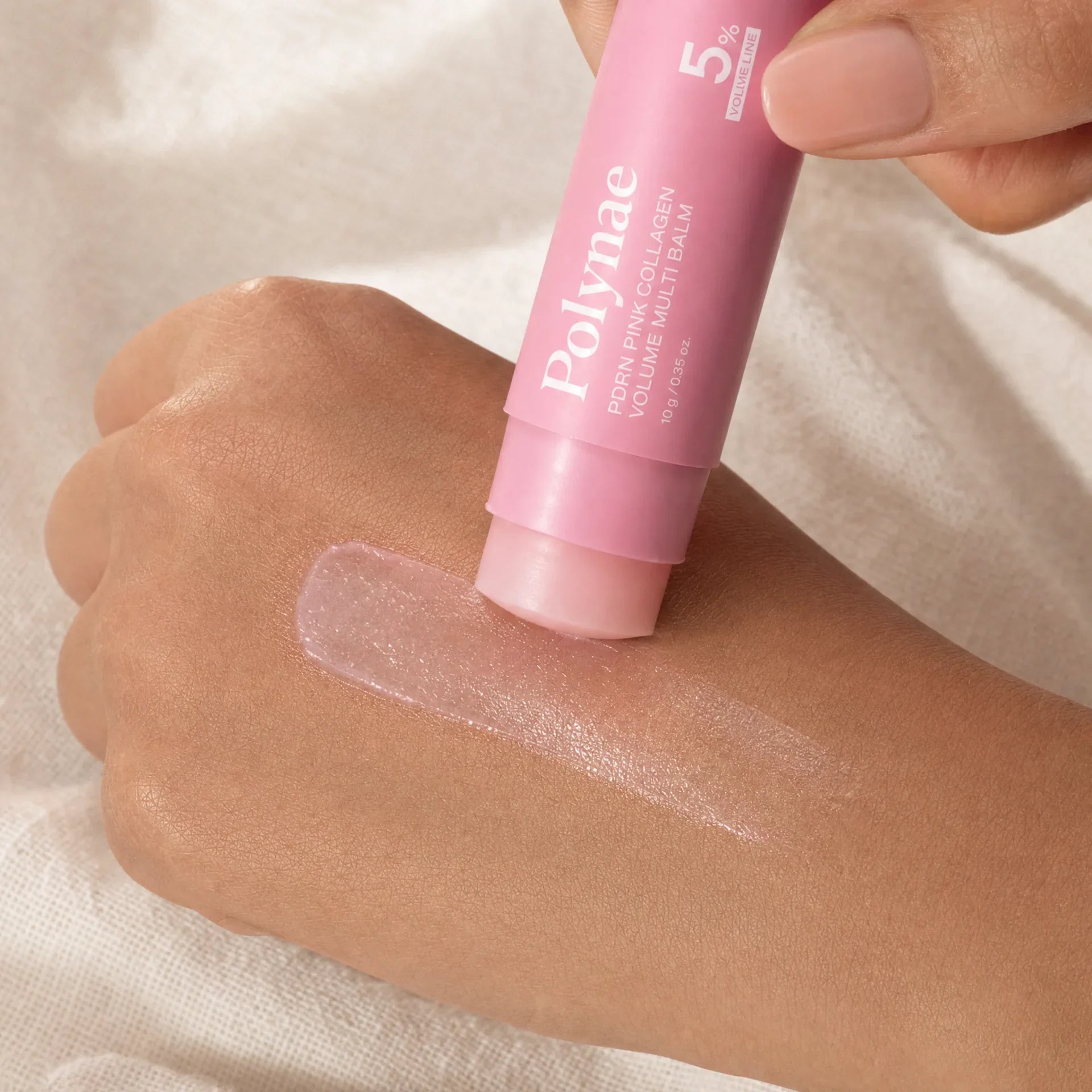 Close-up of the Polynae balm stick being swiped across the back of a hand with a sheer pink glassy texture trail visible on medium-toned skin
